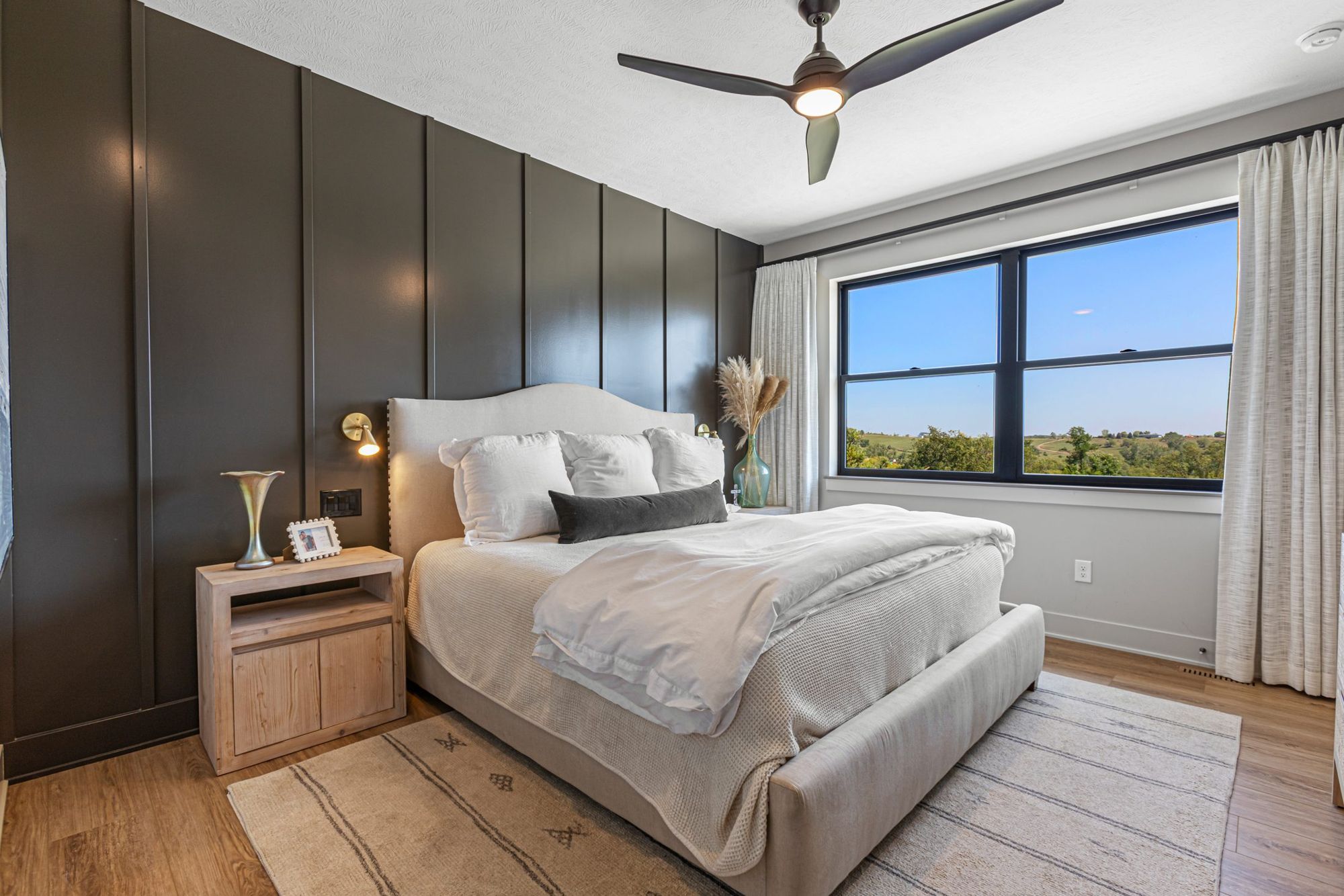 Primary bedroom with dark paneled wall and a window to the fields