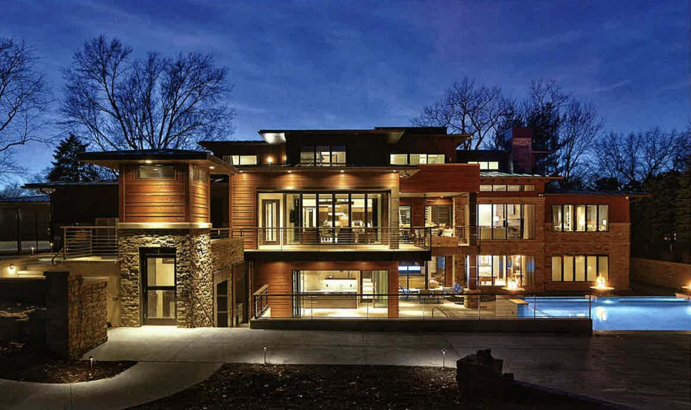Westside Residence, Omaha: a three-level contemporary-rustic home at dusk with stone, timber and a lit pool terrace